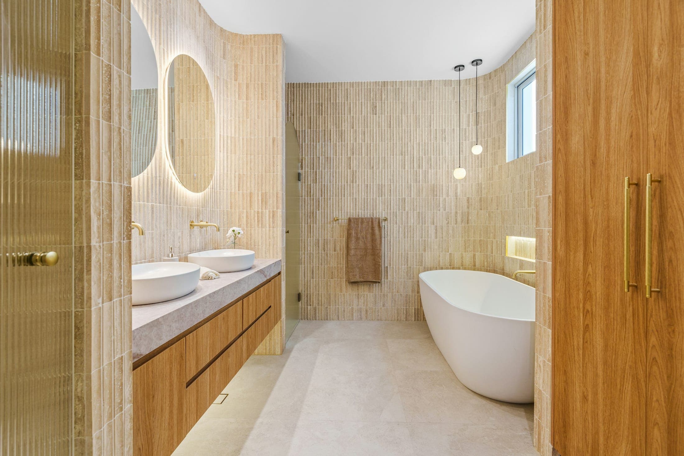 Bathroom with finger-tile walls, a timber double vanity, brass tapware and a freestanding bath
