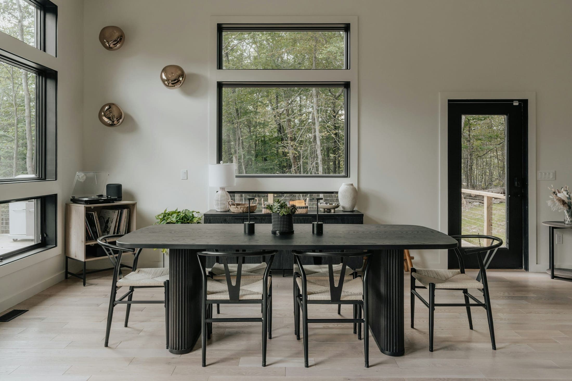 Light-filled dining area with a black fluted table, wishbone chairs and large black-framed windows