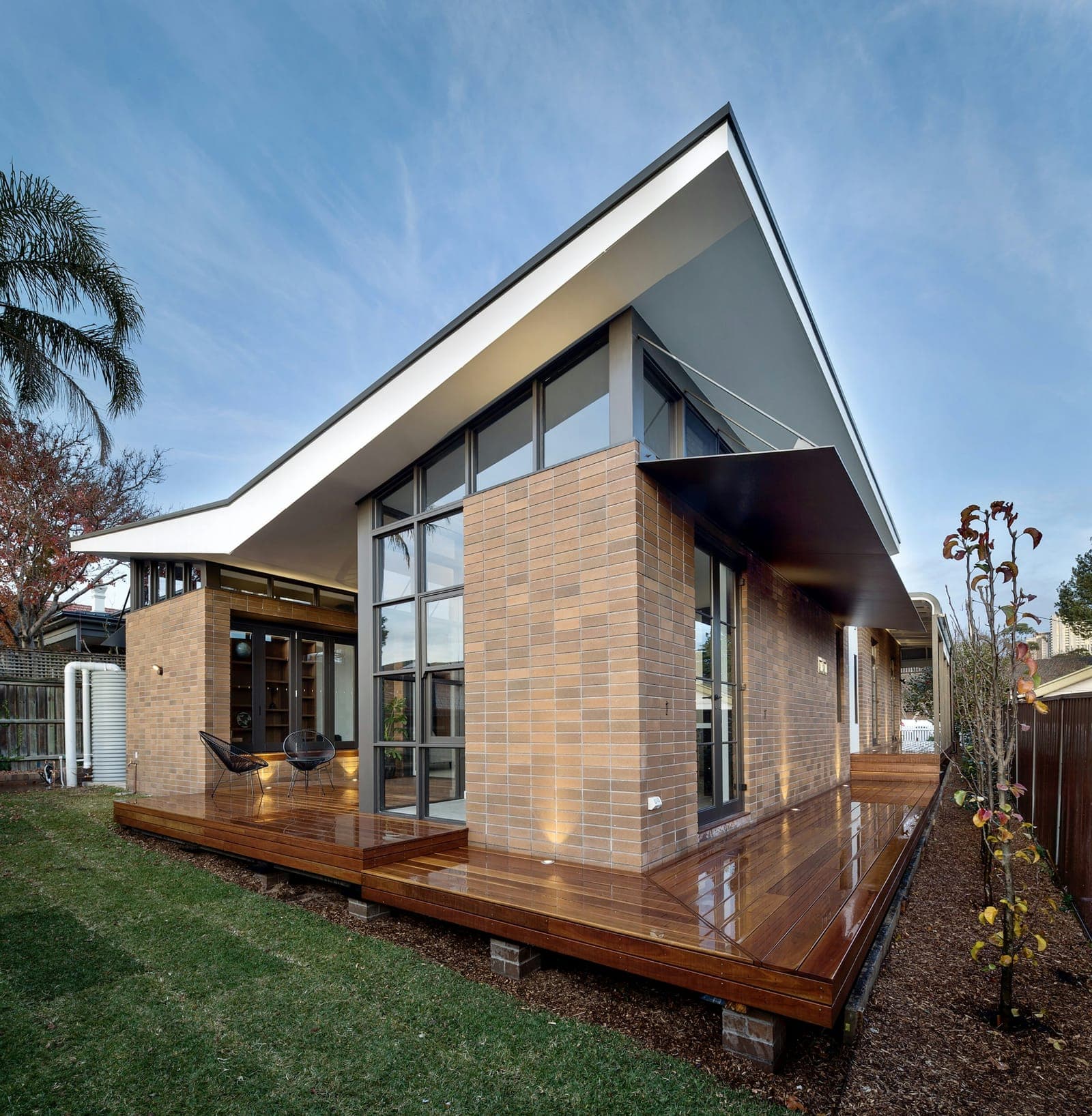 Contemporary brick home with a raked skillion roof, full-height glazing and a timber deck under blue sky