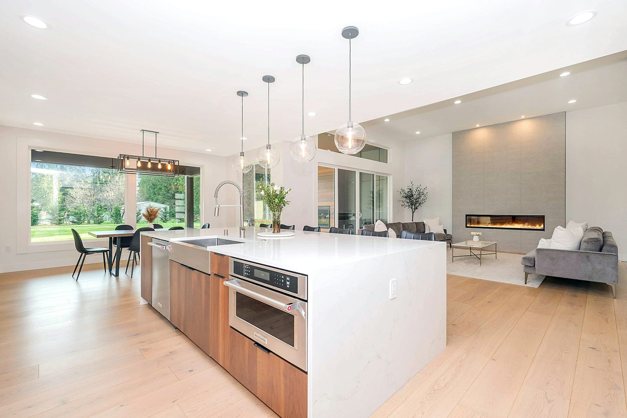 Open-plan kitchen with a white stone waterfall island, timber cabinets and light oak floors