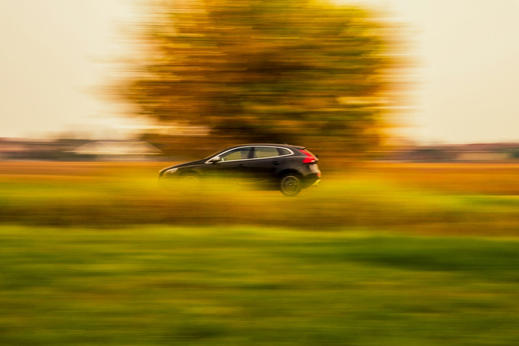 Dark hatchback driving past a field at golden hour with a motion-blurred background
