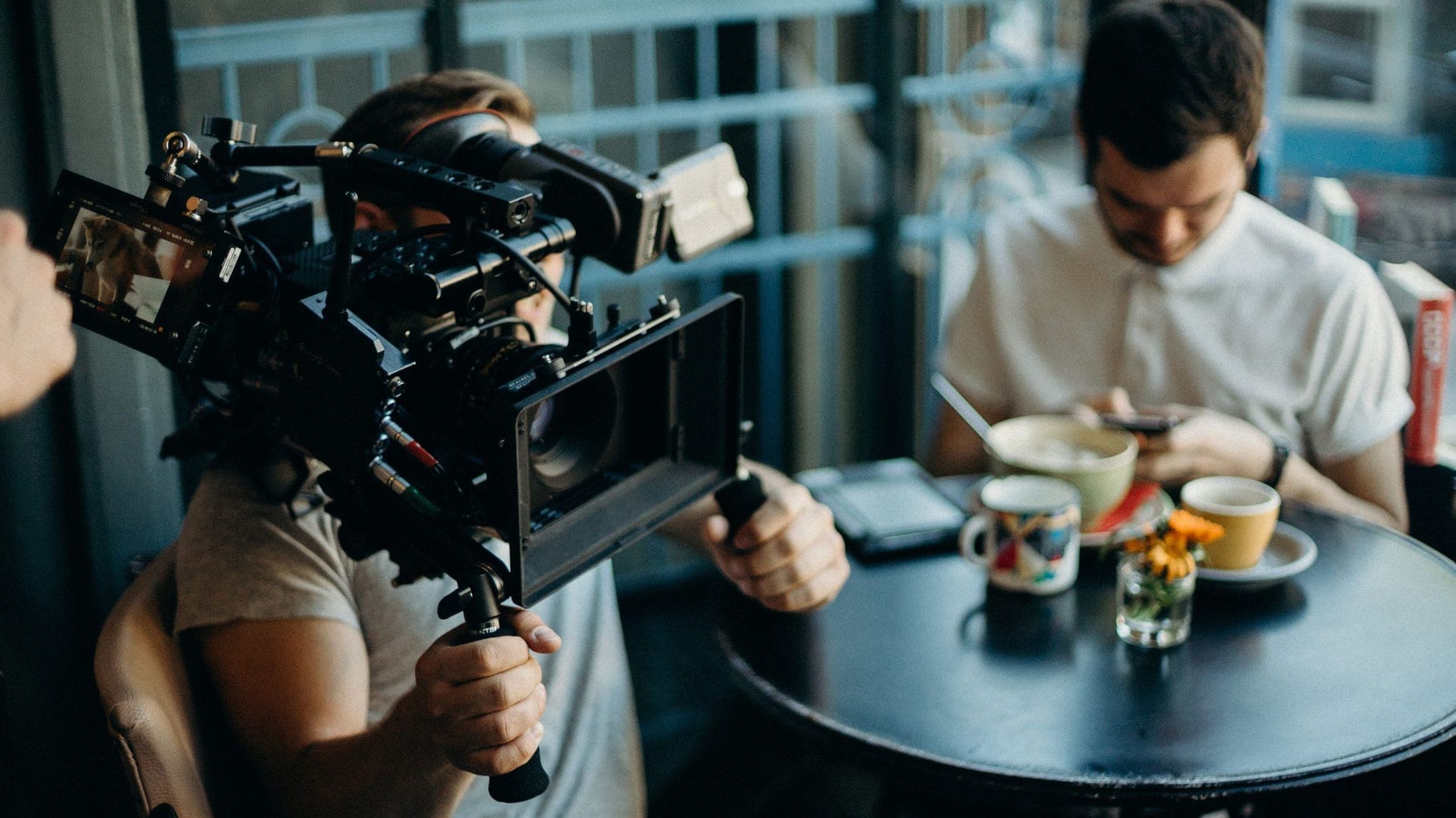Camera operator with a rigged cinema camera filming a man at breakfast in a cafe