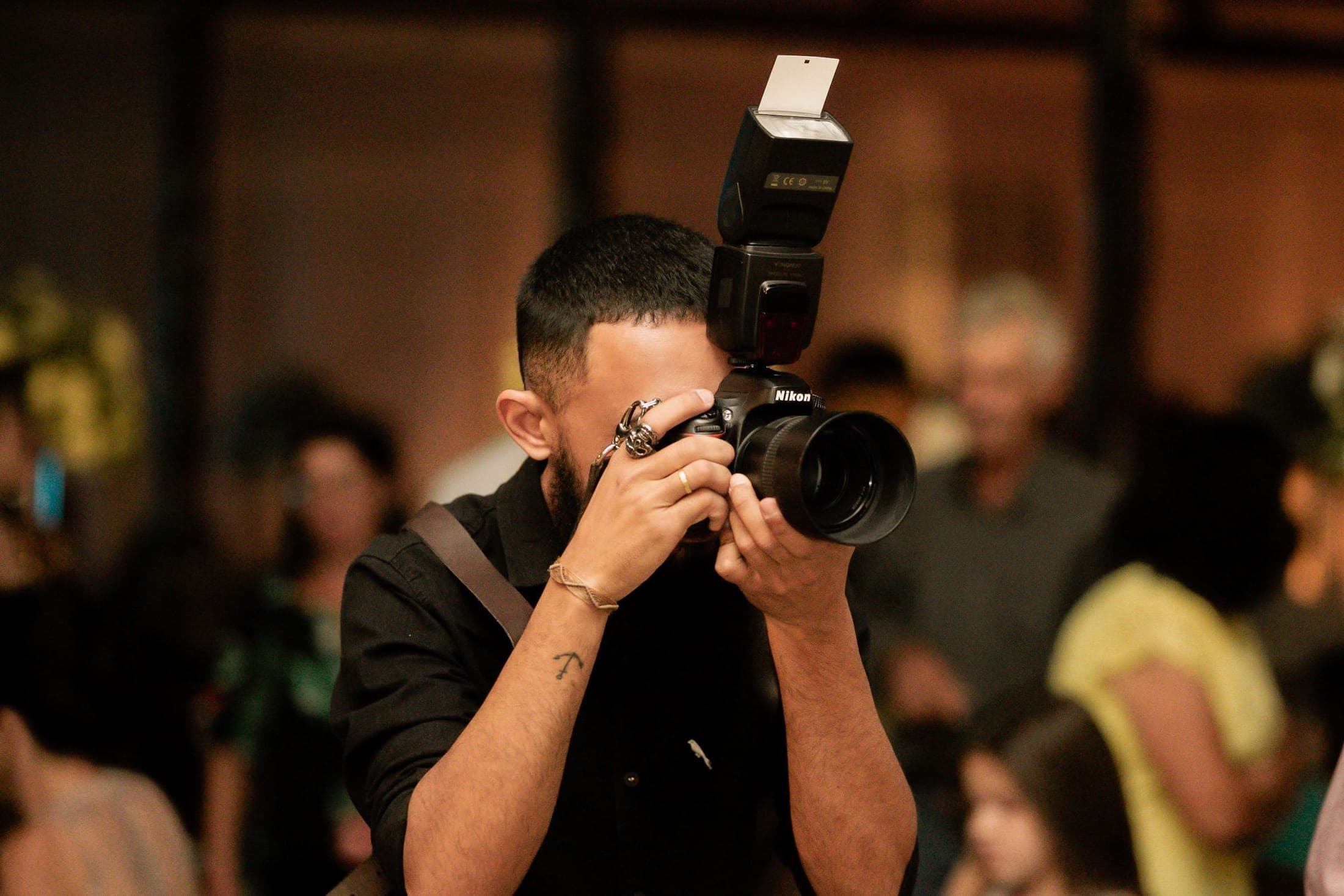 Event photographer with an on-camera flash shooting into a warmly lit crowd