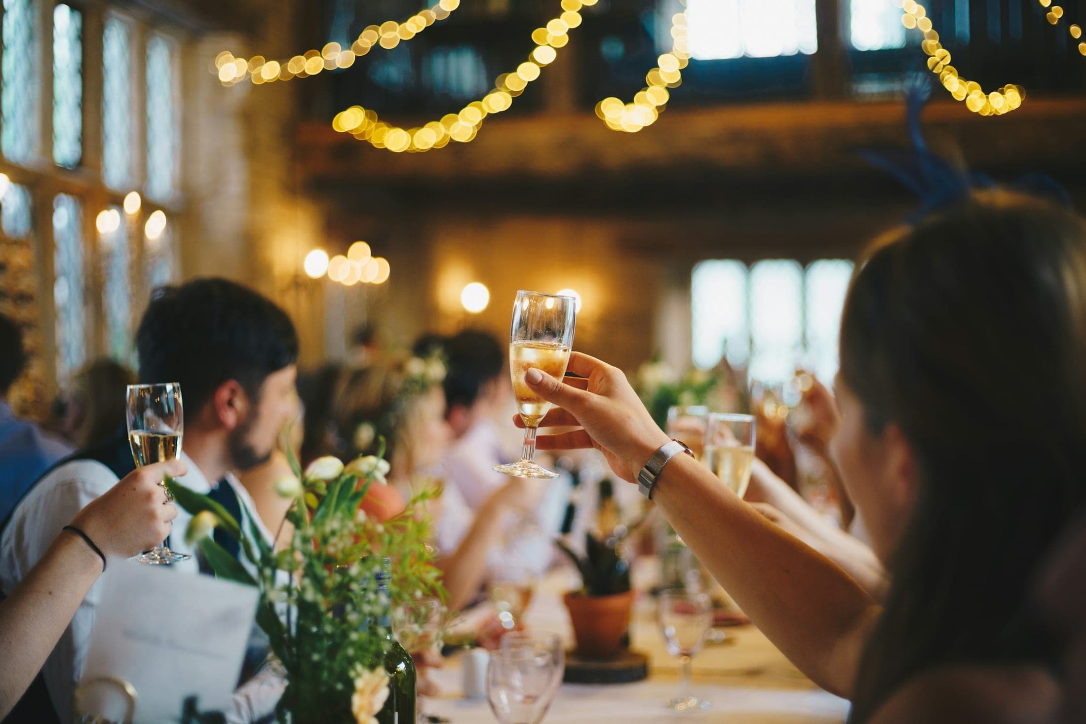 Guests at a long table raising glasses under warm fairy lights