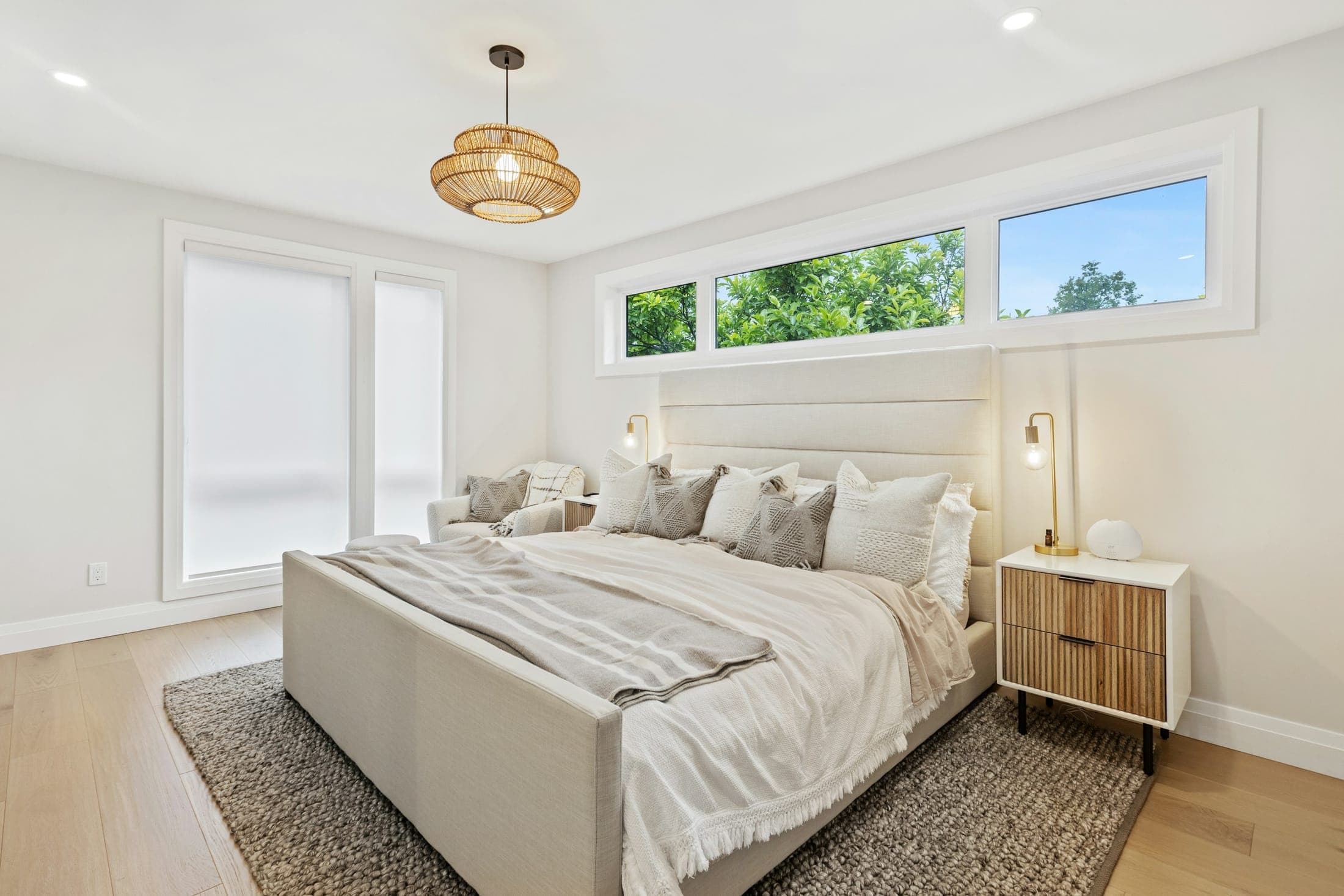 Light-filled main bedroom with an upholstered bed, rattan pendant and a long clerestory window