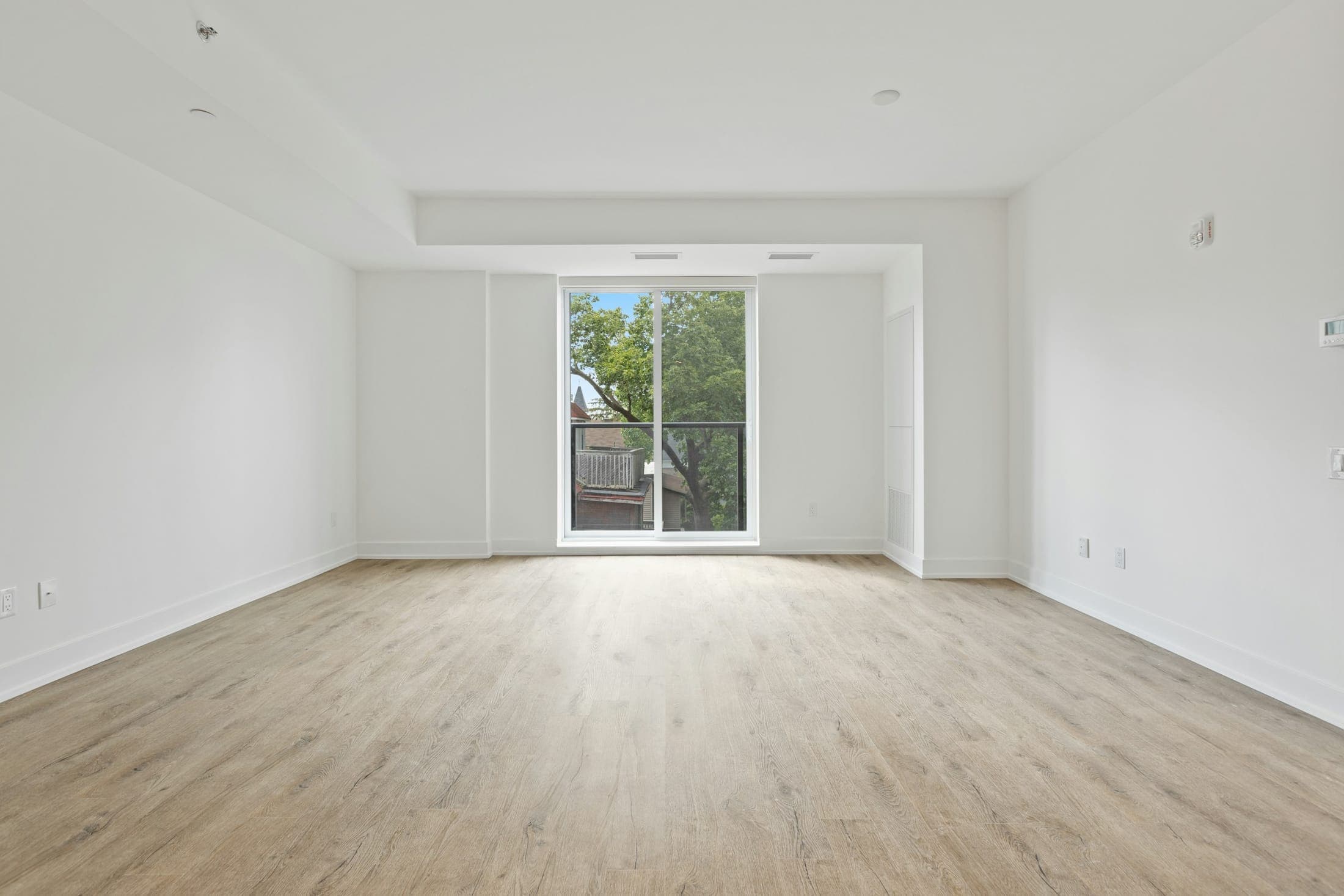 The same living room empty, with light timber-look floors, white walls and a tall glass door