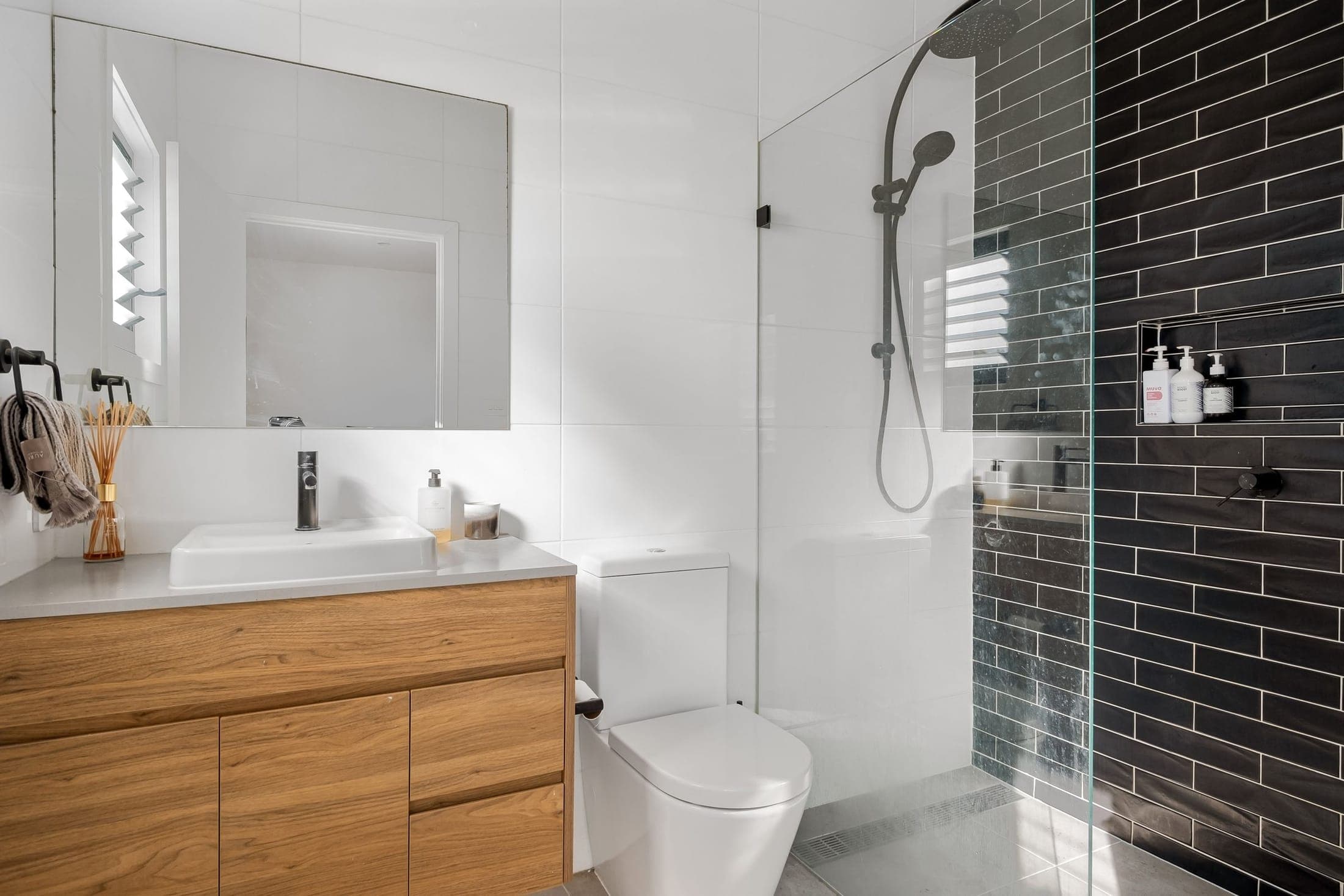 Compact ensuite with a timber vanity, frameless shower and a charcoal subway-tile wall