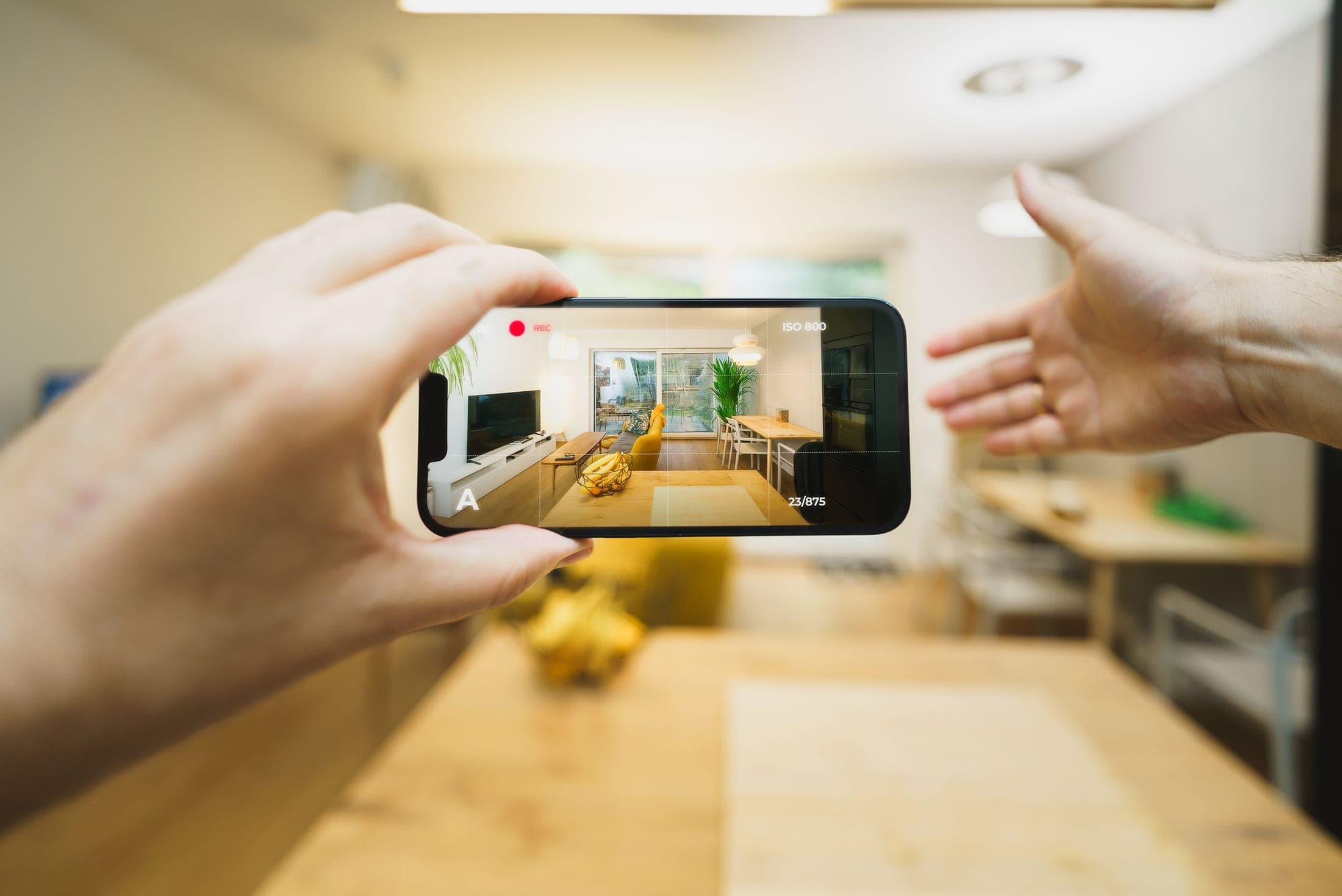 Hand holding a phone recording video of a bright living room